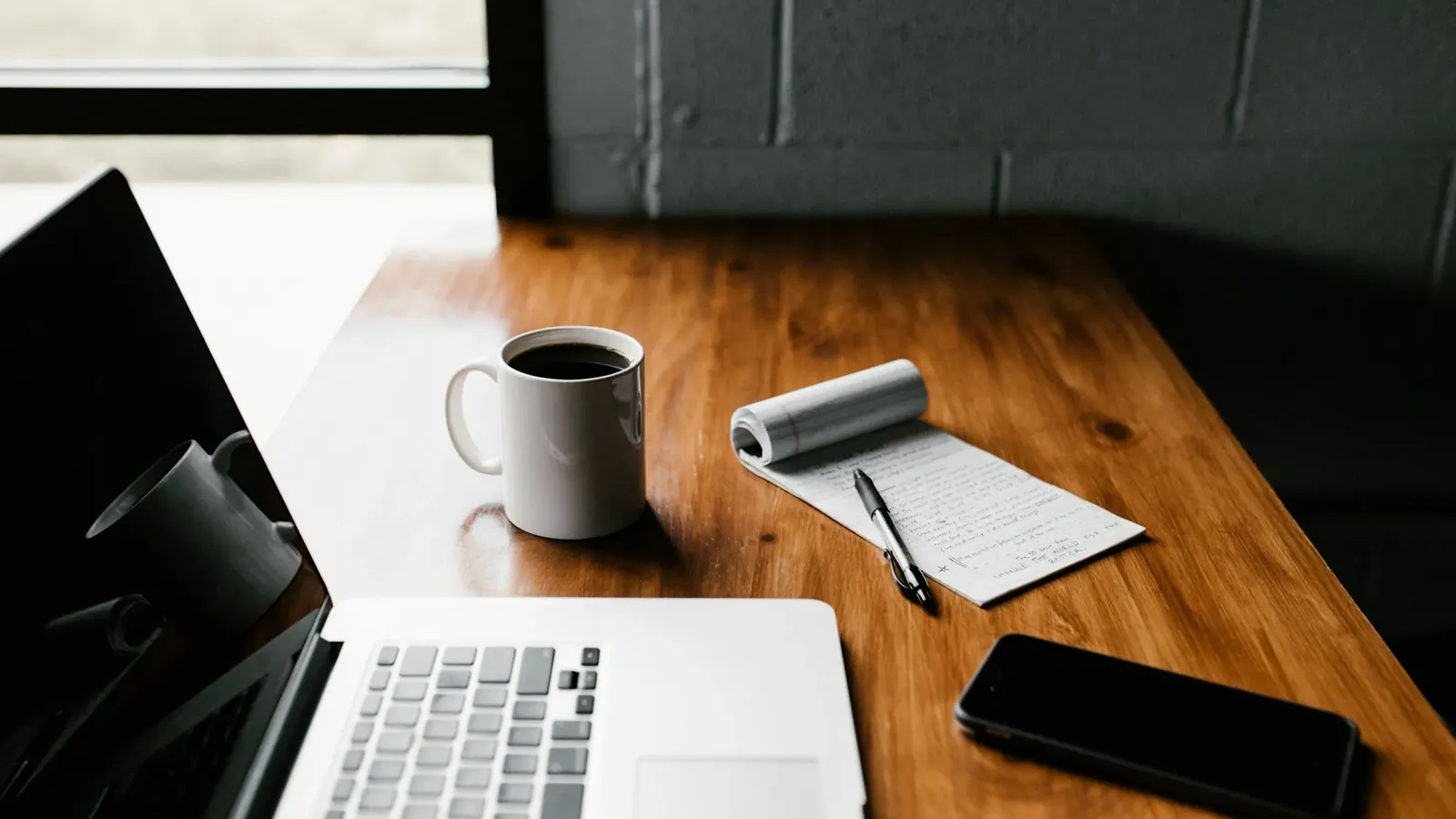 A laptop, a notepad and a coffee on a desk.
